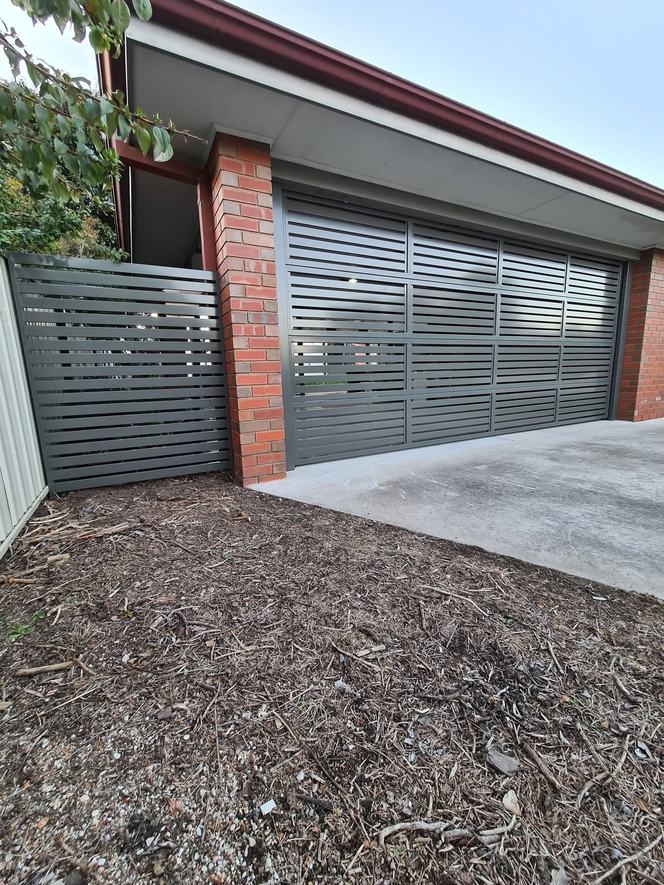 Grey slat sliding gate beside a matching double garage door
